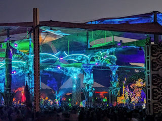 Psychedelic night at Boom Festival in Portugal—luminescent art structures, neon-lit canopies, and a sea of festival-goers united by pounding electronic music and creative energy.