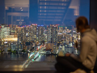 Tokios glittering nighttime skyline, riverfront towers, illuminated bridge, layered reflections, and a quiet observer at the window, amid Japan&rsquo;s luminous urban pulse.