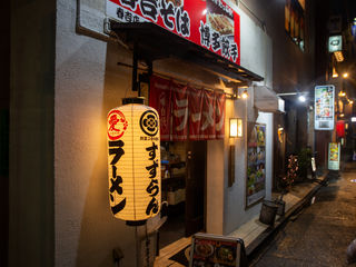 Warm lantern light, red noren curtains, bold Japanese calligraphy, and a narrow Kyushu alley alive with ramen aromas and nighttime intimacy.
