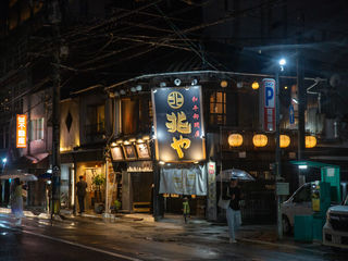 Rain-soaked Japanese alleyway, glowing paper lanterns, intimate traditional restaurant, tangled overhead wires, umbrellas, bicycles, and quiet nighttime streets in Kyushu.