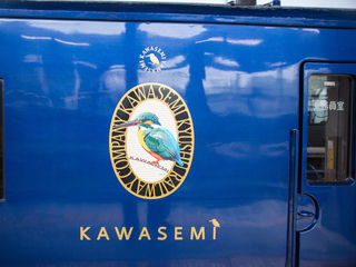 Glossy cobalt carriage, vivid kingfisher emblem, Japanese lettering, and Kawasemi Yamasemi branding—an elegant Kyushu railway journey steeped in regional color.