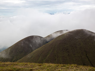 Misty volcanic ridges of Kyushu’s Aso highlands, velvety green-brown grass, drifting cloud sea, distant peaks, and a cool overcast sky.