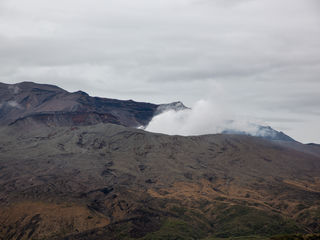 Mount Aso’s vast volcanic slopes, charcoal ridges, and rolling cloud banks beneath a steel-gray Kyushu sky—an austere landscape of fire, wind, and quiet reverence.