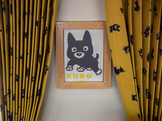 Mustard-yellow curtains with playful black Kuro bears, a rustic wooden sign, and cheerful Aso character—an inviting touch of Kyushu hospitality.