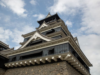 Kumamoto Castle’s towering white-and-black facades, intricate gray-tiled roofs, formidable stone ramparts, and dramatic clouds against a bright Kyushu sky—an enduring symbol of Japan’s samurai heritage.