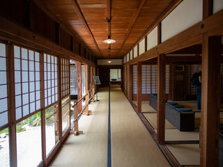 Traditional Japanese corridor in Kyushu, warm cedar beams, shoji screens, tatami floors, lanterns, and a serene garden courtyard beyond.